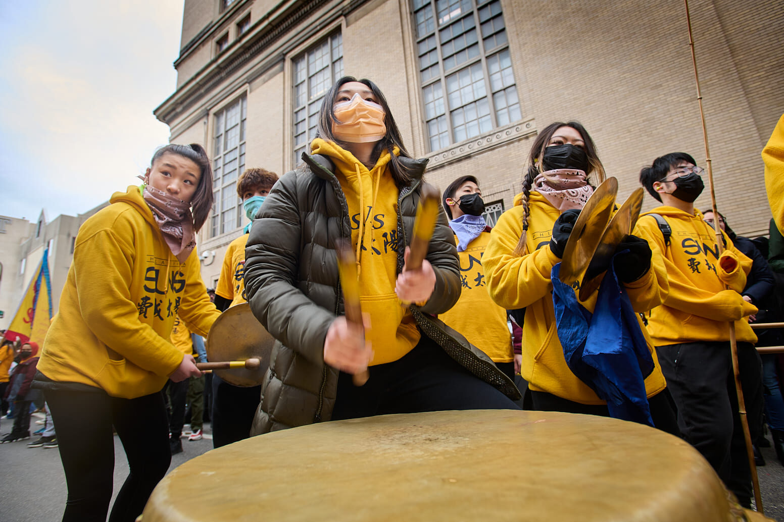 Group of young East Asian individuals wearing face masks playing drums at a street festival